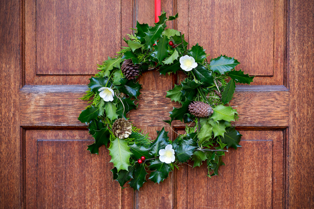 Ghirlanda con agrifoglio e fiori invernali con fuori porta natalizio