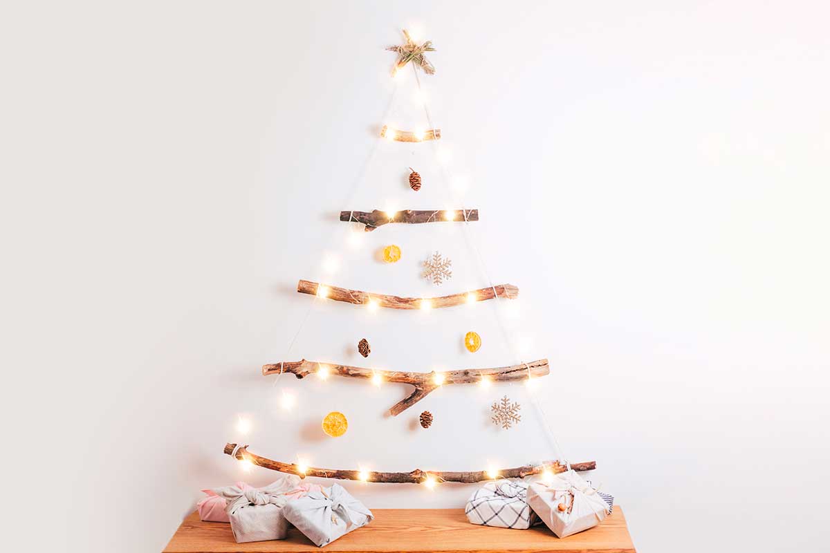L’albero di Natale a parete con legnetti e catene luminose