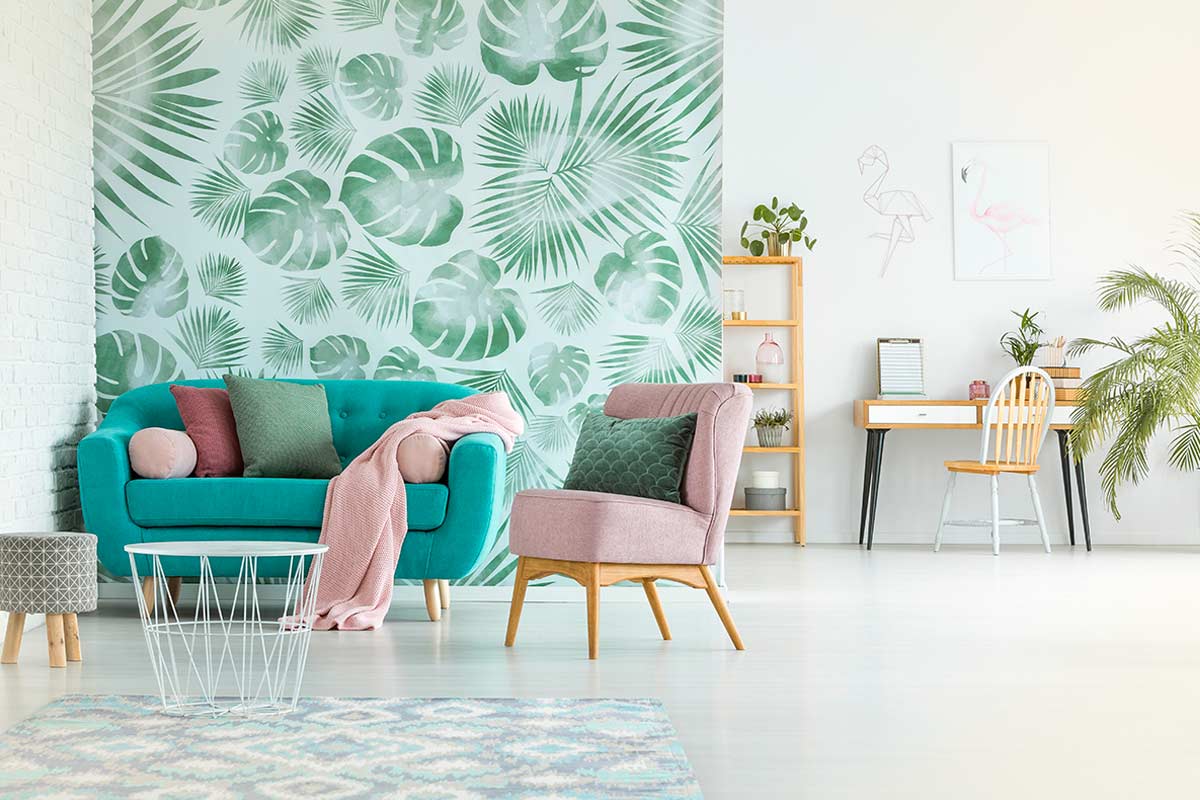 Soggiorno luminoso con carta da parati a foglie tropicali verde acqua, divano turchese, poltrona rosa cipria e angolo studio moderno con piante