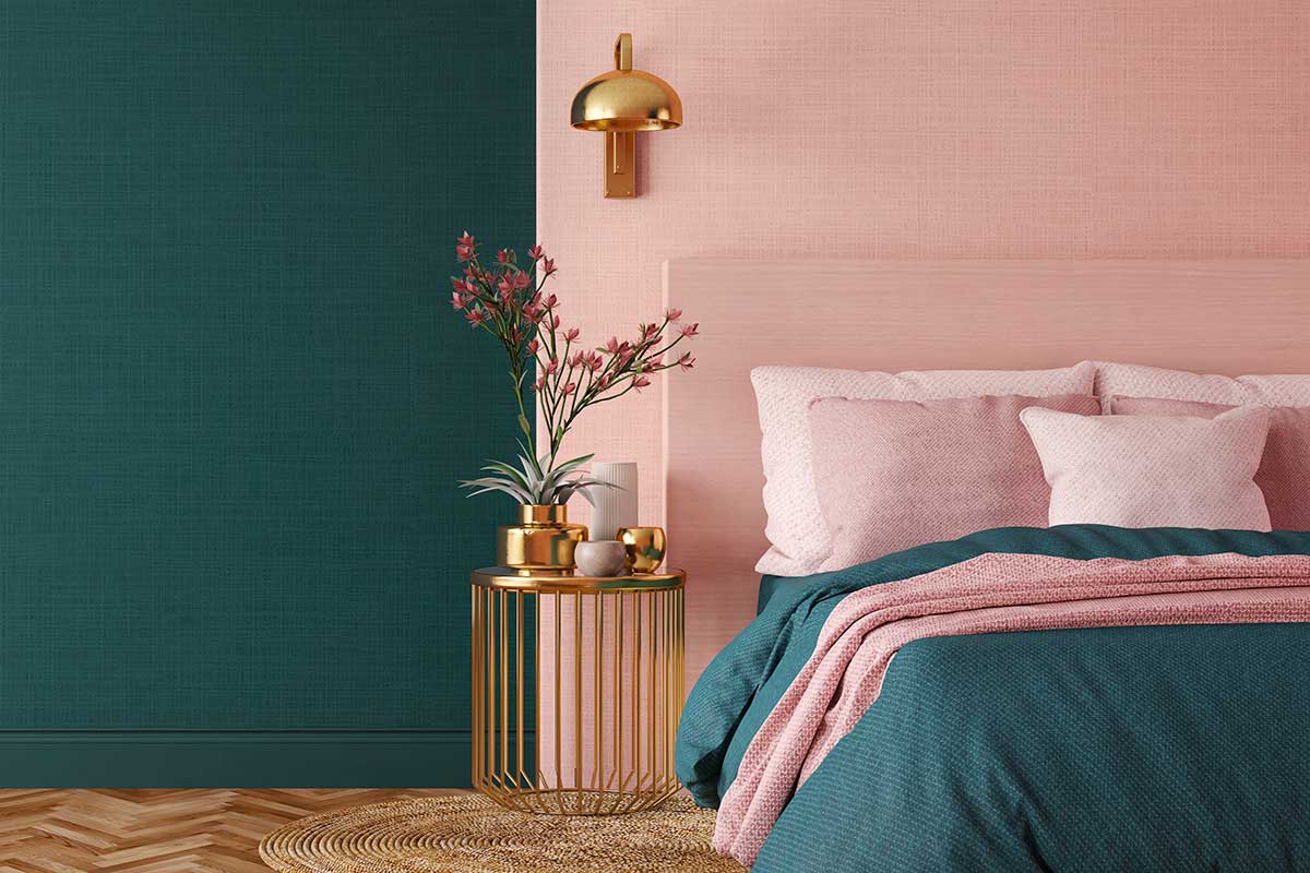 Camera da letto moderna con parete verde petrolio e rosa cipria, biancheria coordinata nei toni pastello e dettagli in oro. Tavolino rotondo con vaso di fiori e lampada dorata, parquet chiaro a spina di pesce, atmosfera elegante e rilassante.