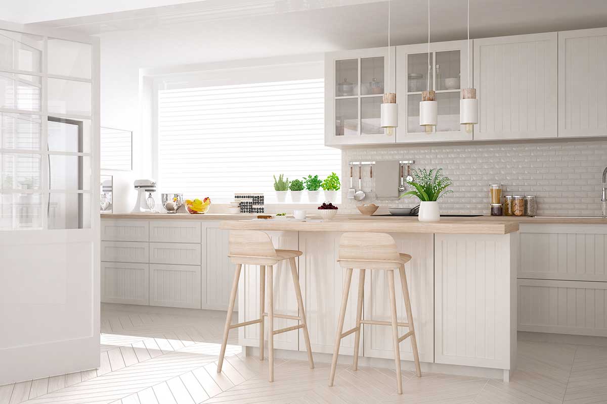 Cucina minimal moderna in bianco e legno chiaro con isola centrale, sgabelli alti, piante aromatiche e luce naturale abbondante. Atmosfera luminosa, accogliente e ordinata.