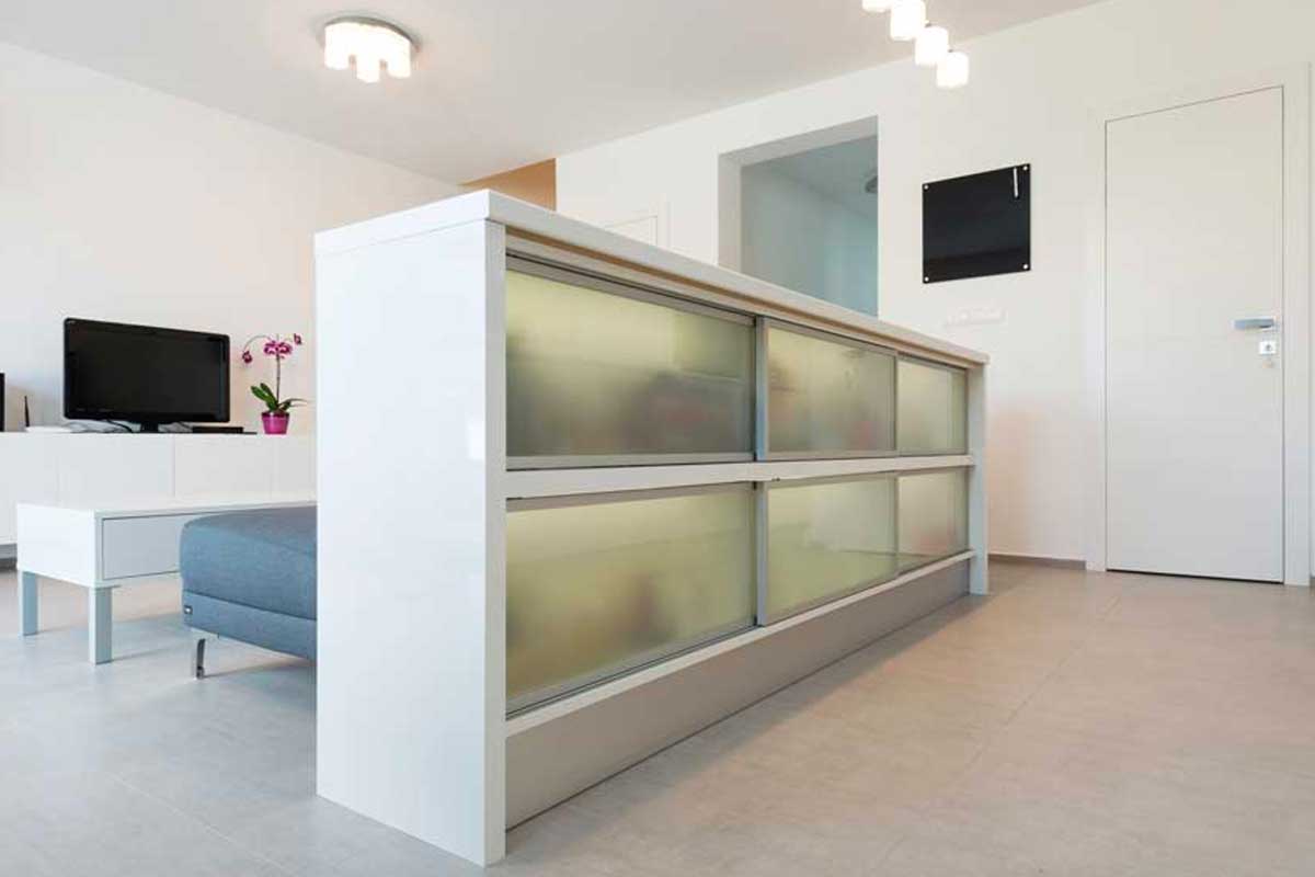 Mobile basso bianco con vetro satinato usato come divisorio tra cucina e soggiorno in un open space moderno.