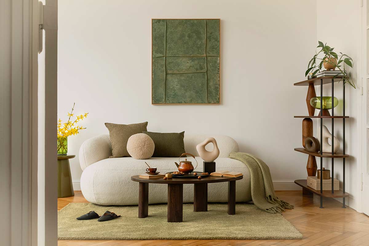 Salotto moderno e luminoso, divano chiaro, quadro materico verde su parete, mensola con piante e dettagli in legno.