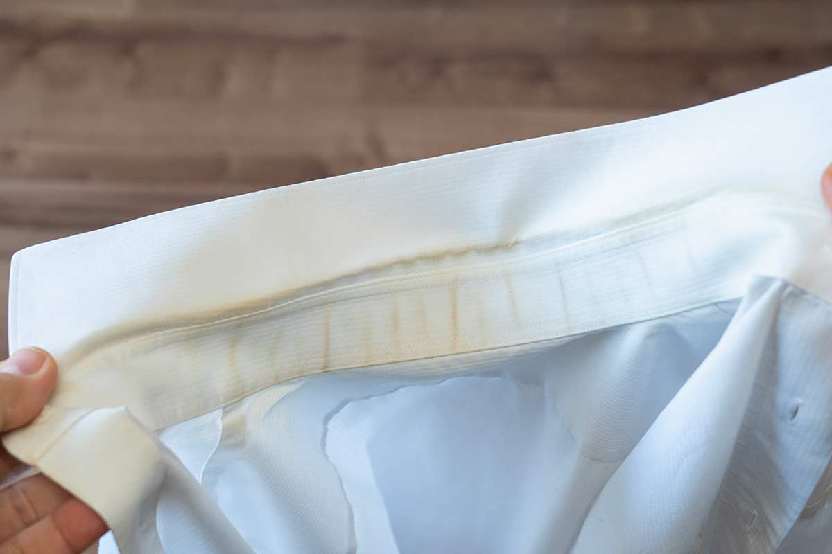 Colletto di camicia bianca con evidente alone giallastro e macchie di sudore, segno tipico di ingiallimento dopo ripetuti lavaggi e uso di candeggina.