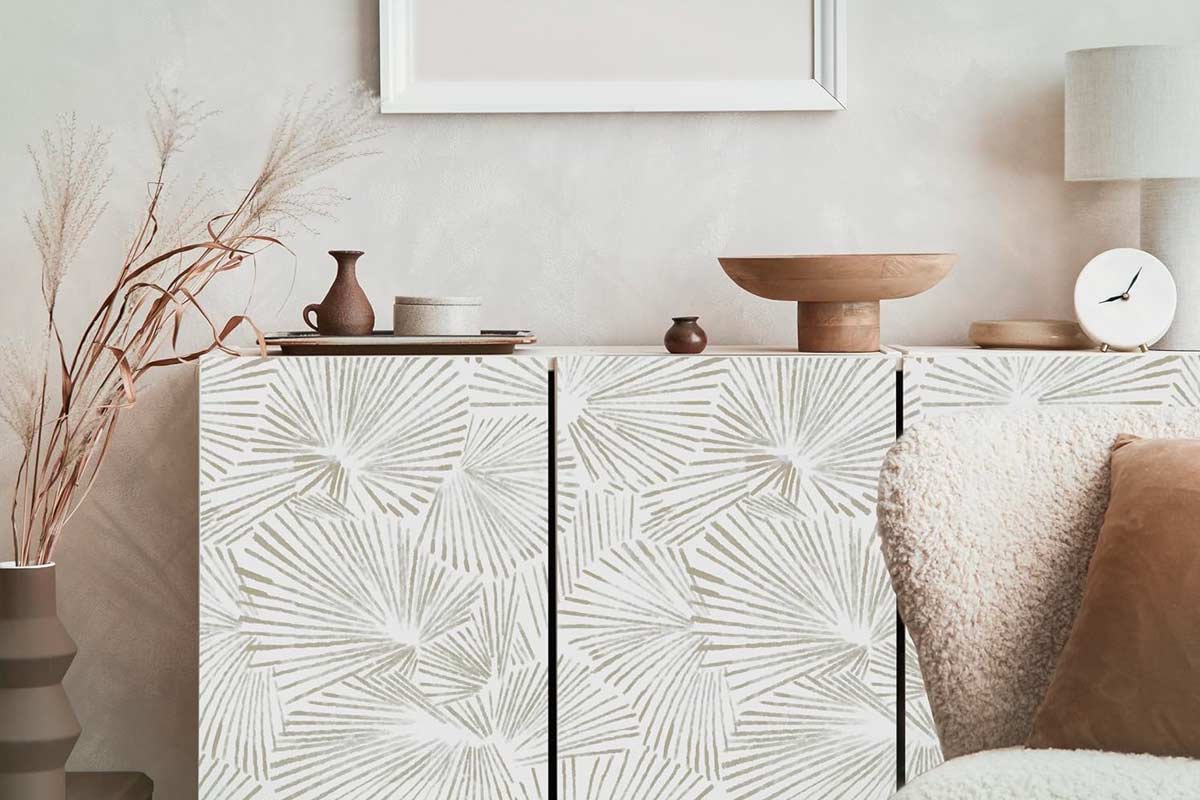 Madia moderna rivestita con carta da parati chiara a motivo grafico di palmette stilizzate, in un ambiente neutro con dettagli in ceramica, legno naturale e tessuti bouclé. Sul mobile, vasi minimal e oggetti decorativi, atmosfera soft e nordica.