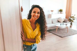 Donna sorridente con camicia gialla in casa luminosa e ordinata, esempio di ambiente più spazioso dopo il decluttering.