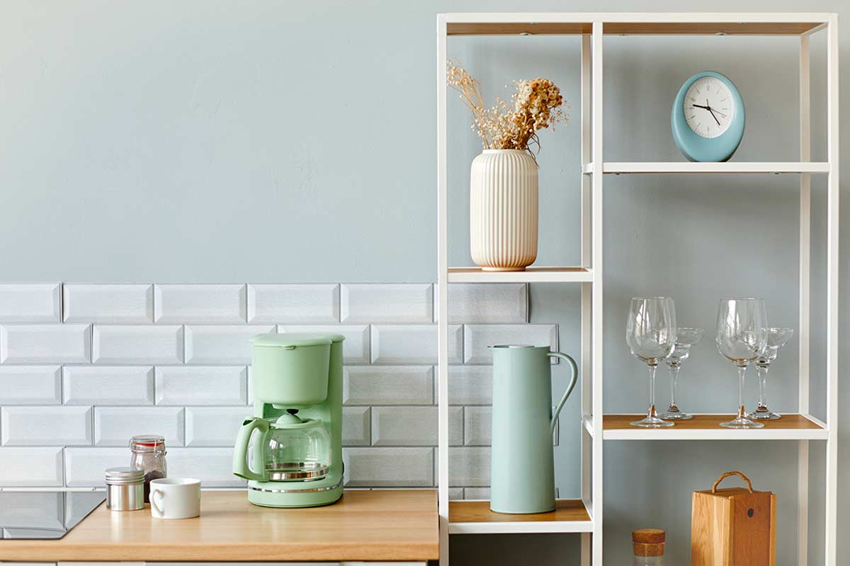 Cucina moderna bianca e legno con parete verde salvia chiaro, piastrelle bianche a mattoncino, accessori in verde pastello e dettagli naturali.