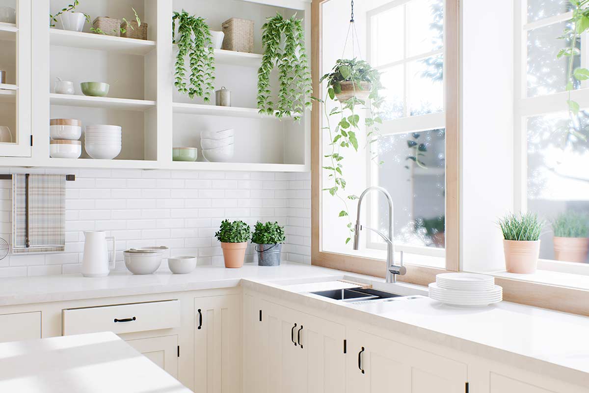 Cucina luminosa con superfici bianche, piante aromatiche in vaso sul piano e davanzale, mensole ordinate con stoviglie e oggetti neutri, rubinetto moderno vicino a una grande finestra che lascia entrare molta luce naturale. Nessun elemento fuori posto, atmosfera ordinata e accogliente.