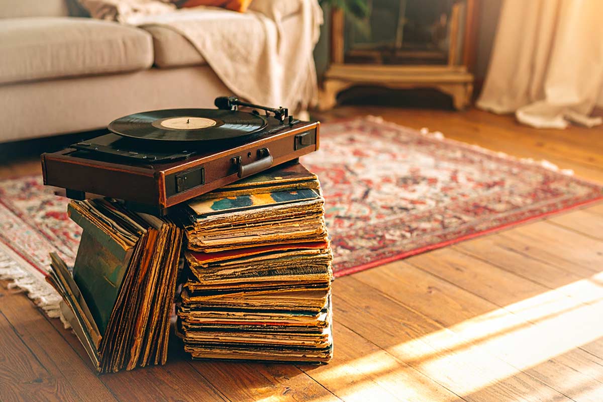 Giradischi vintage appoggiato su una pila di vecchi vinili, in un soggiorno con tappeto orientale e pavimento in legno, illuminato dalla luce naturale.
