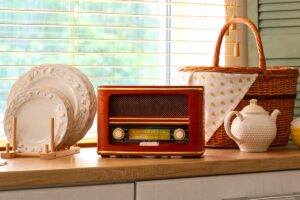 Radio vintage in legno su mensola di cucina, tra piatti in ceramica bianca e cestino intrecciato.
