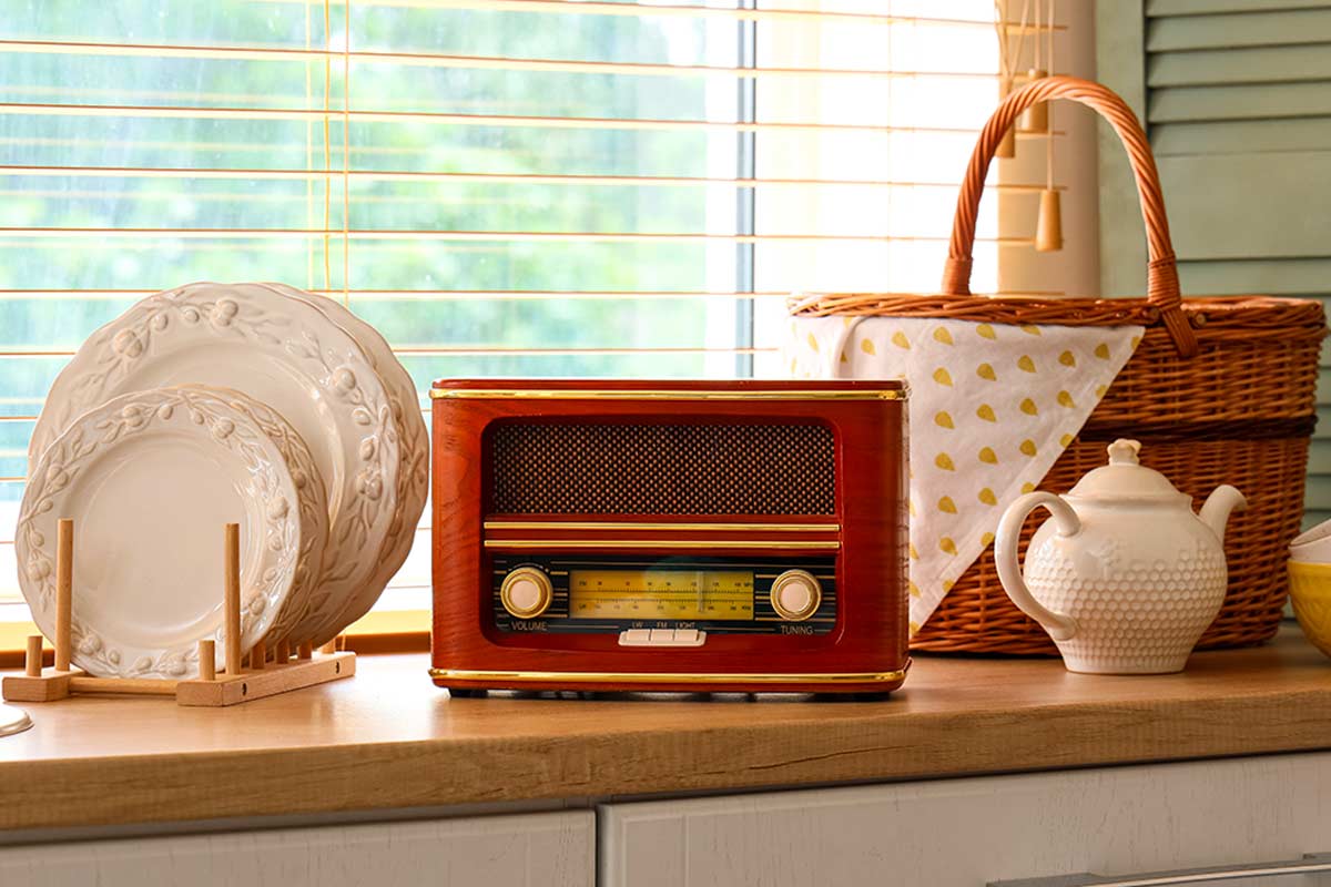 Radio vintage in legno su mensola di cucina, tra piatti in ceramica bianca e cestino intrecciato.