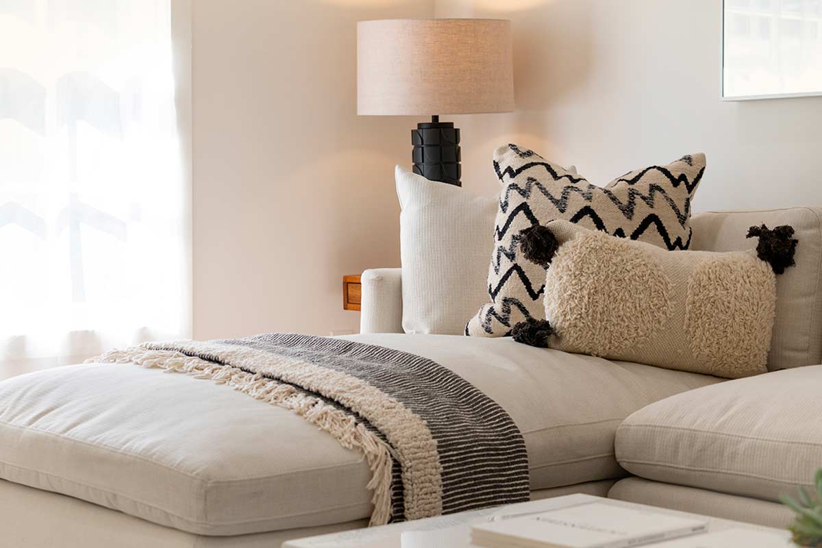 Living minimalista in toni avorio, con tessuti stratificati e luce naturale filtrata da tende leggere.