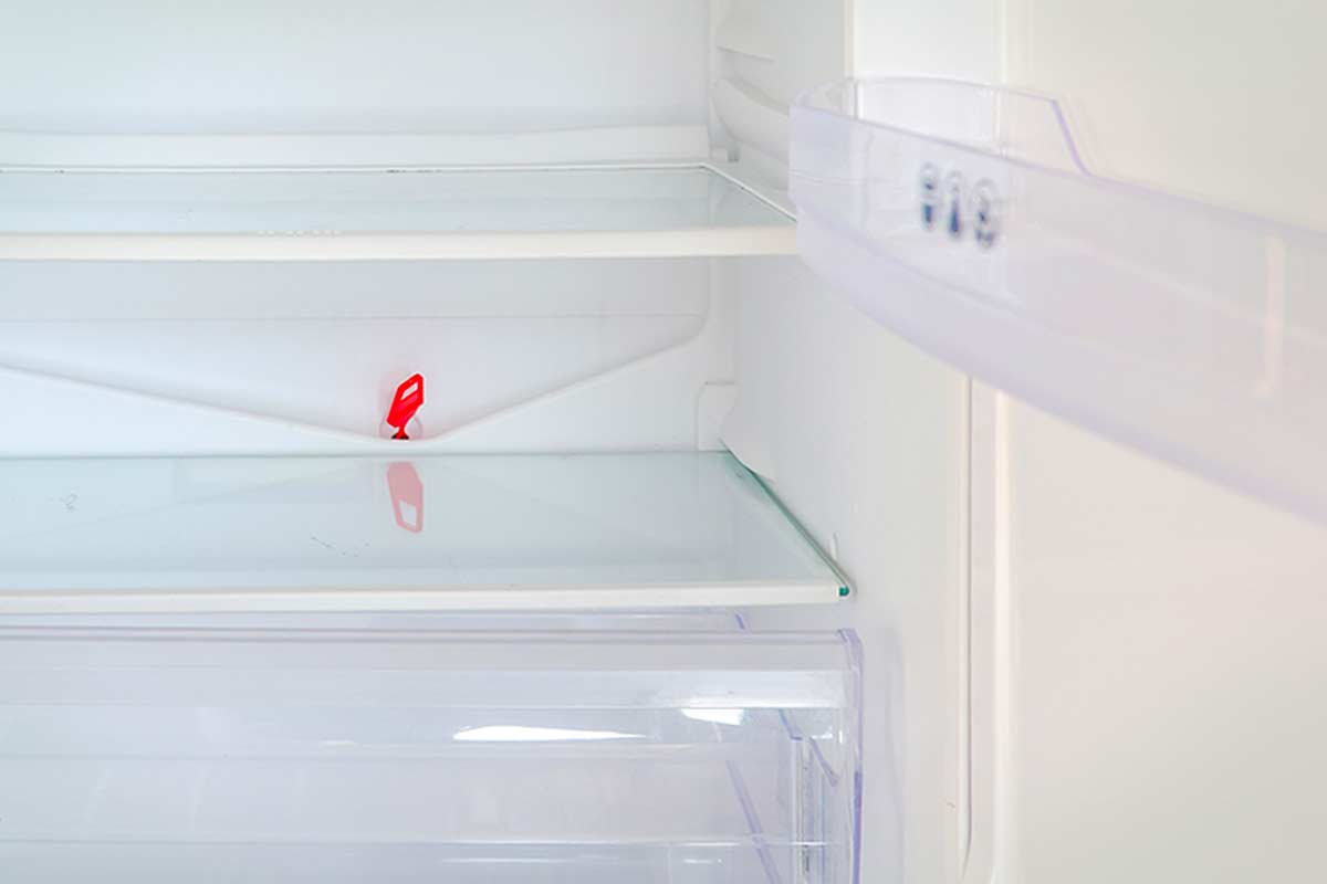 Primo piano del foro di scolo all’interno di un frigorifero vuoto, evidenziato da una linguetta rossa in plastica.