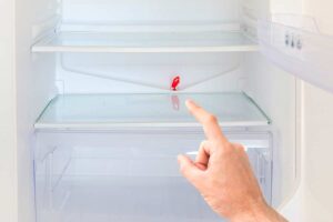 Mano indica il foro di scolo interno di un frigorifero, punto critico per la formazione di odori sgradevoli, foto: © Pavlo Vakhrushev - Stock adobe