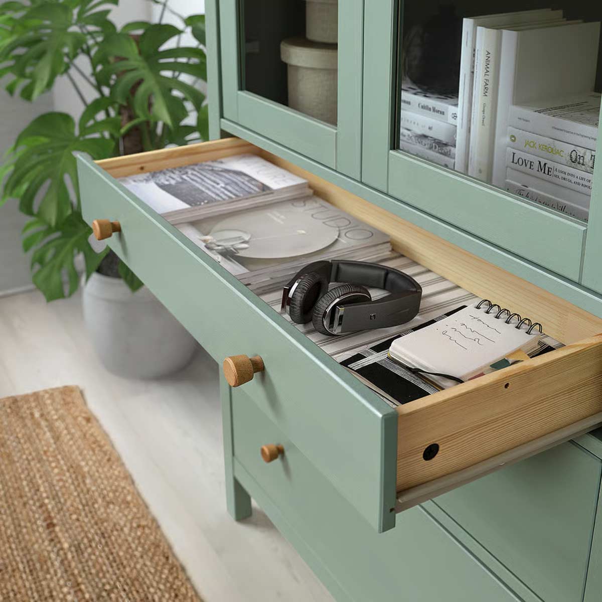 Cassetto HEMNES verde salvia aperto con riviste, cuffie e taccuino, dettagli in legno massiccio e pianta sullo sfondo.