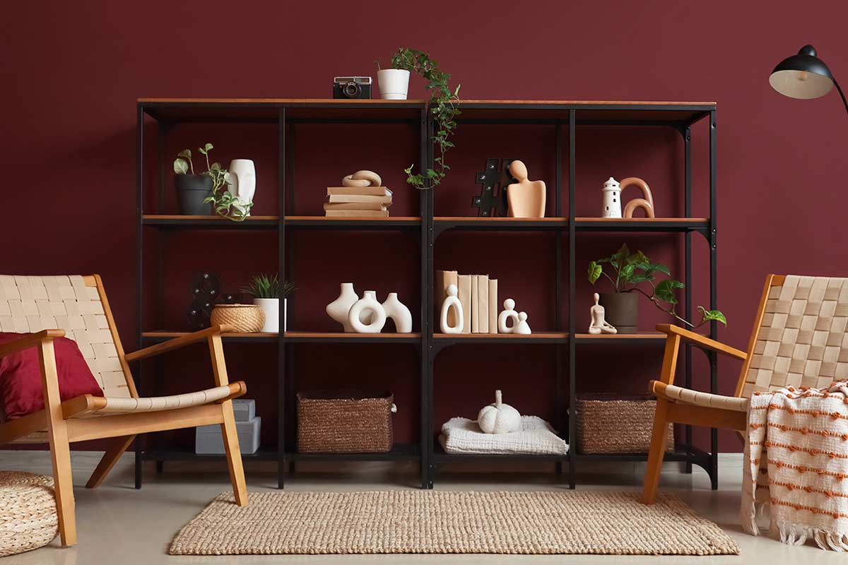 Libreria con oggetti e libri disposti in piccoli gruppi dispari su fondo bordeaux, esempio di regola del 3 e spazi vuoti nell’arredo.