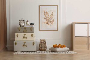 Angolo di soggiorno moderno con valigie vintage impilate usate come tavolino, decorazioni botaniche a parete, cuscino con pompon e tappeto a motivi geometrici.