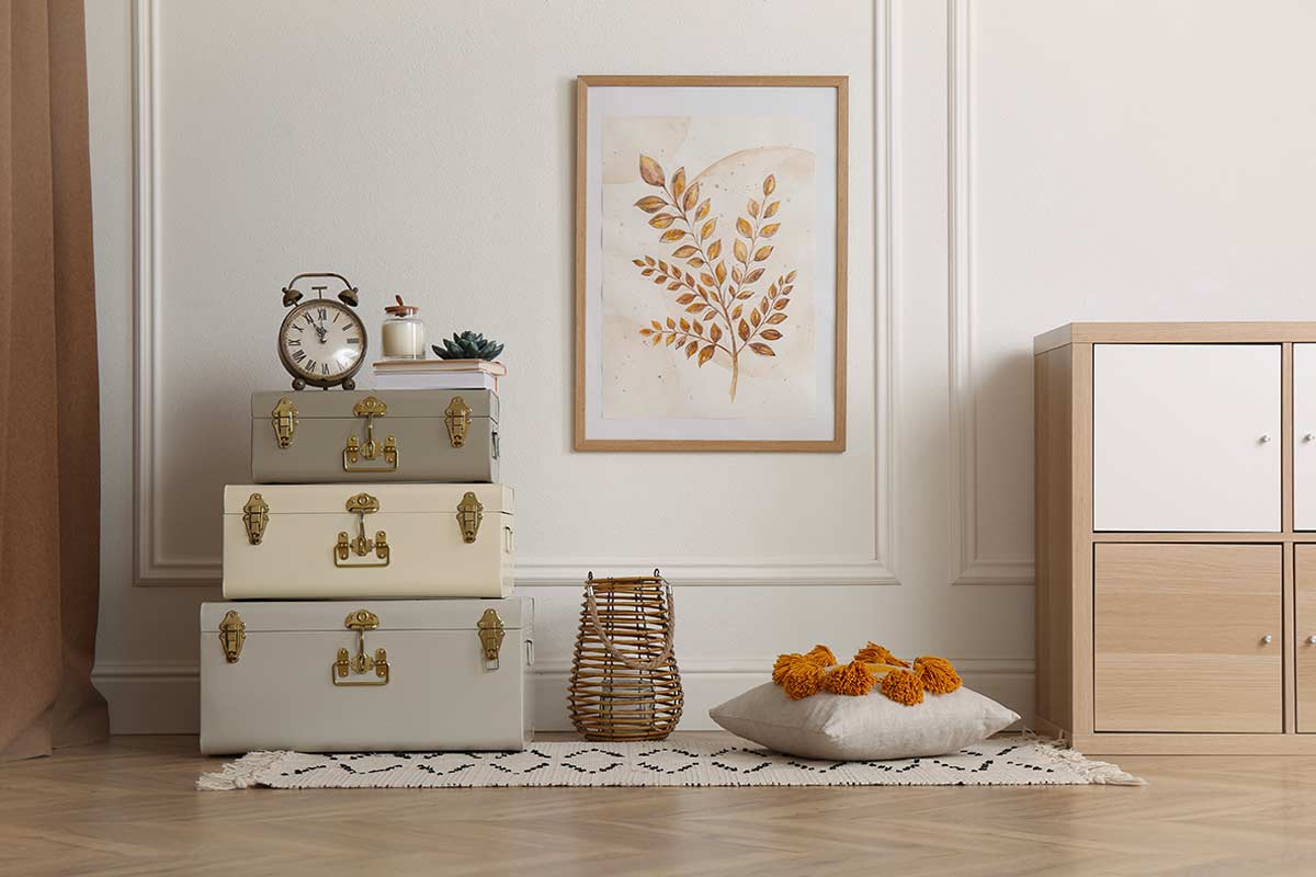 Angolo di soggiorno moderno con valigie vintage impilate usate come tavolino, decorazioni botaniche a parete, cuscino con pompon e tappeto a motivi geometrici.