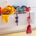Cassetto di armadio bianco aperto con vestiti colorati e una scarpa rossa che pende fuori, segno di disordine nell’armadio dei bambini.