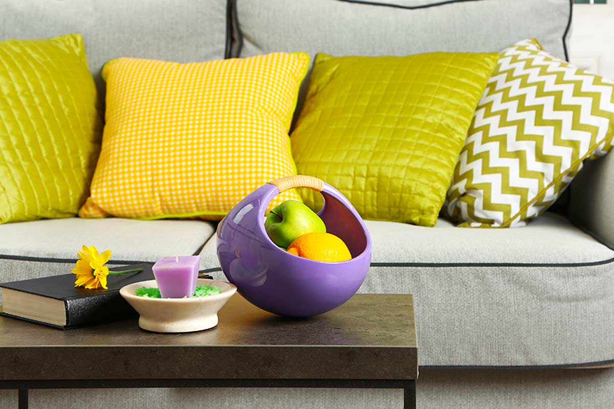 Ciotola malva su tavolino davanti a divano con cuscini gialli e verdi.