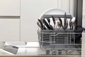 Dettaglio di posate in acciaio con aloni bianchi e macchie di corrosione causate dal sale della lavastoviglie.