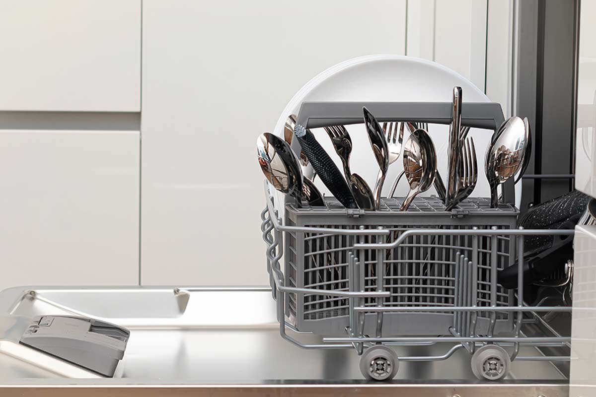 Dettaglio di posate in acciaio con aloni bianchi e macchie di corrosione causate dal sale della lavastoviglie.