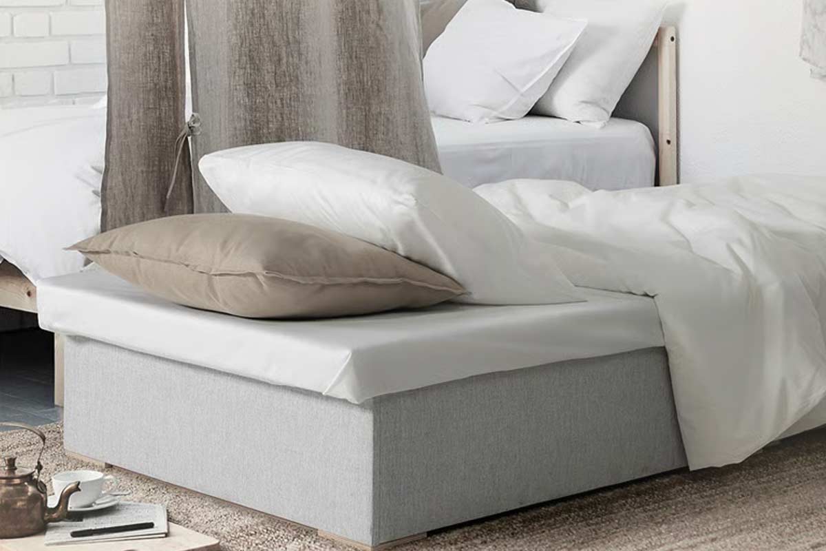 Pouf letto IKEA BURSERYD aperto in modalità letto, con lenzuola bianche e cuscino, posizionato in una camera dal look minimal e luminoso.