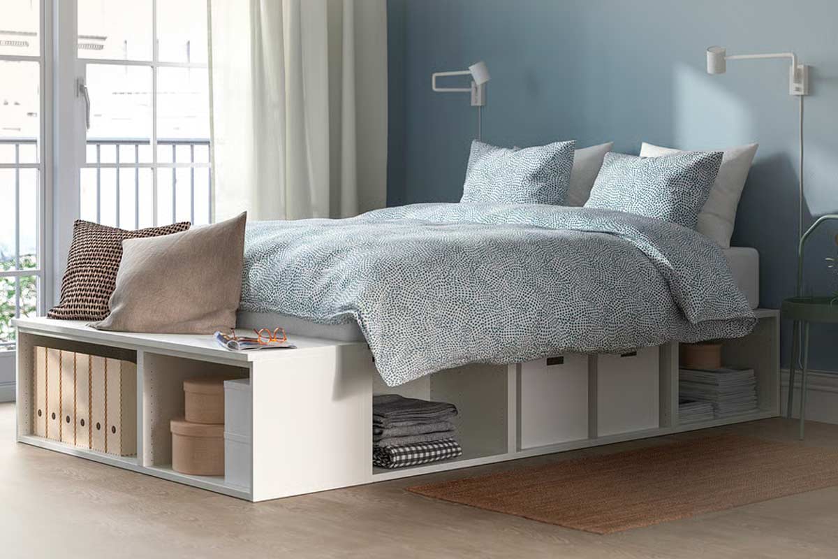 Letto contenitore IKEA PLATSA in una camera piccola con pareti azzurre, biancheria a motivi, spazio organizzato nei vani laterali e luce naturale che entra dalla finestra.