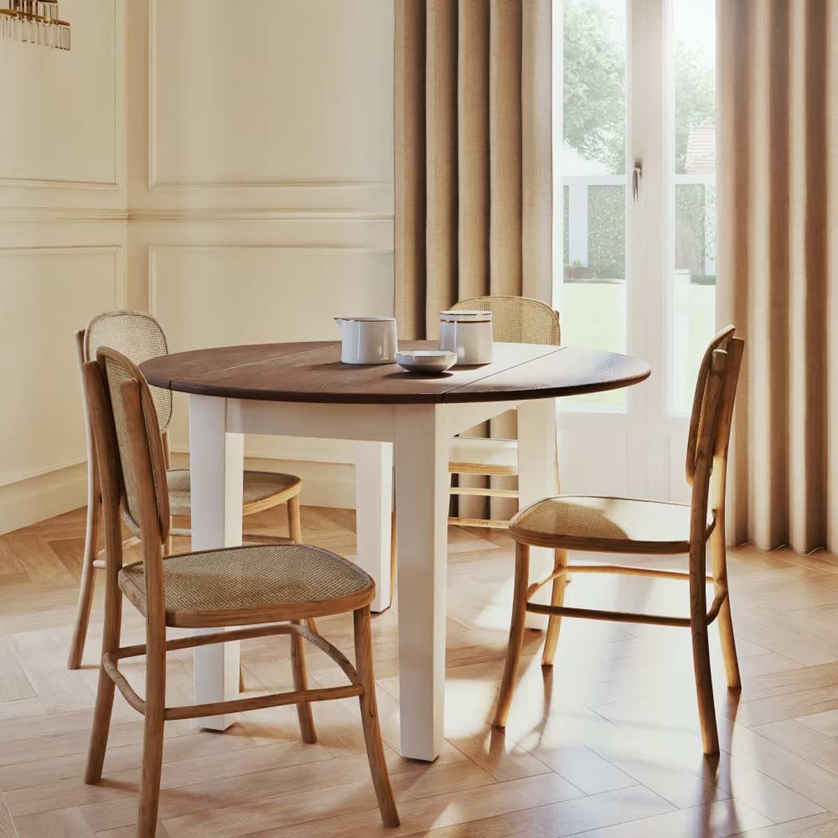 Tavolo Provence di Maisons du Monde in versione rotonda, apparecchiato per la colazione in una sala luminosa, con sedie in legno e seduta intrecciata.