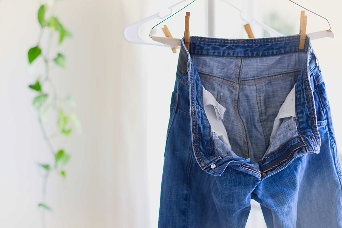 Pantaloni di jeans stesi su una gruccia in plastica, fissati alle estremità con mollette, in ambiente domestico luminoso.