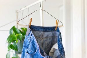 Jeans appesi a rovescio per l’orlo con mollette sulle cuciture laterali, su una gruccia in metallo, per favorire la stesura senza pieghe.