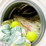 Pallina da tennis inserita nel cestello della lavatrice con un piumino bianco per ridare volume.