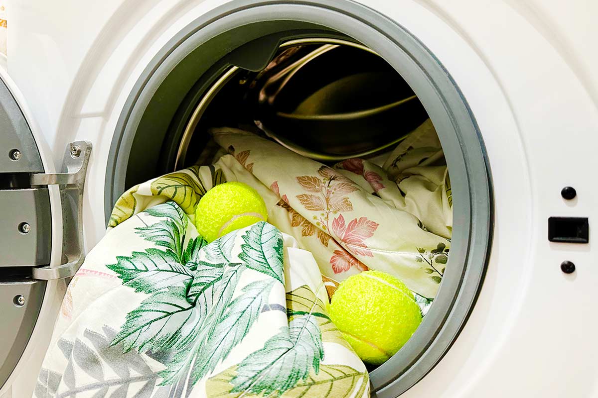 Pallina da tennis inserita nel cestello della lavatrice con un piumino bianco per ridare volume.