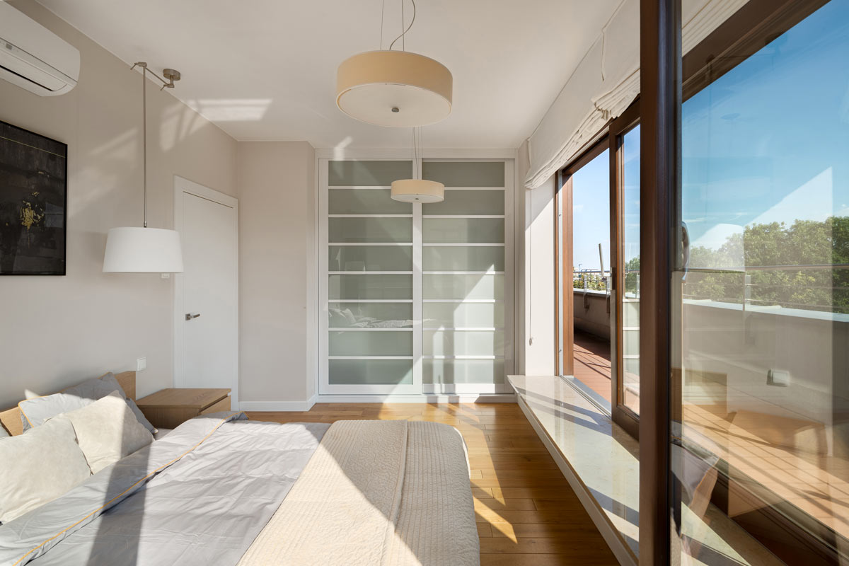 Armadio a muro con ante scorrevoli bianche in una camera moderna e luminosa con parquet e grandi finestre.