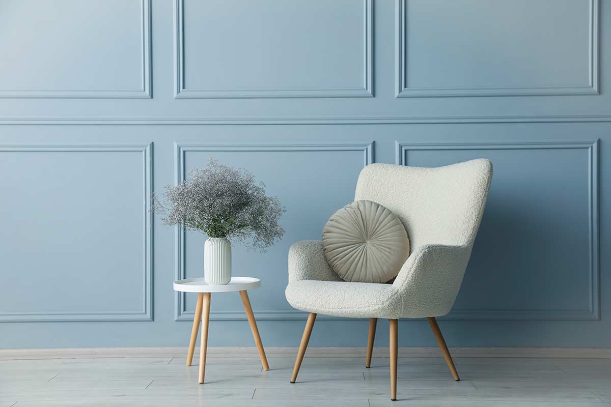 Poltrona chiara e tavolino su sfondo di parete blu polvere con boiserie.
