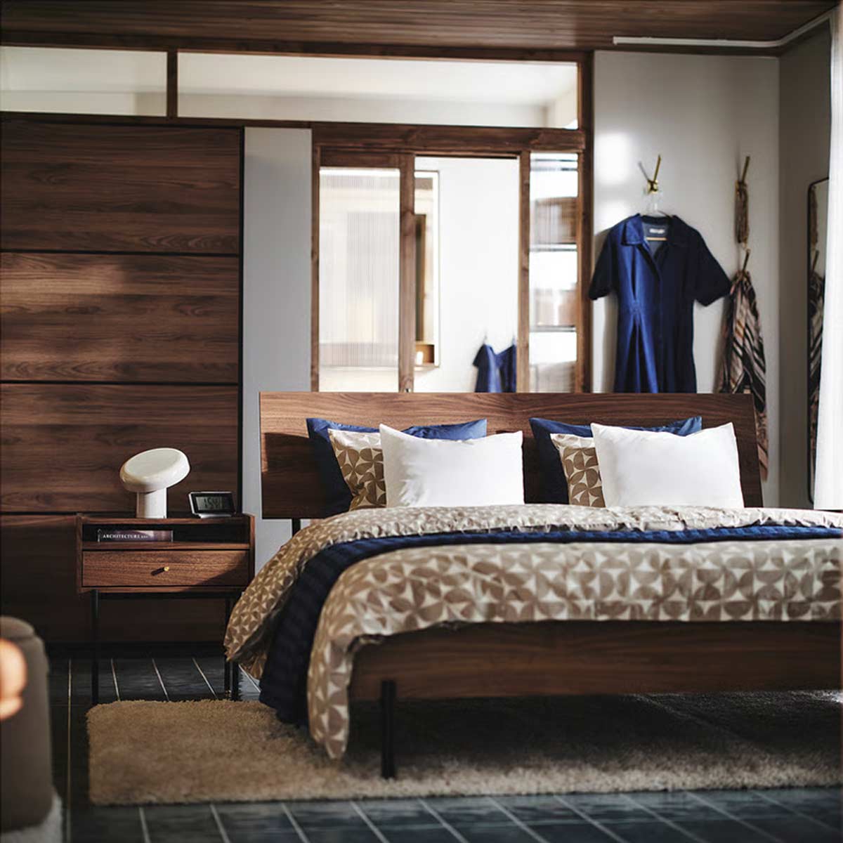 Camera da letto moderna con mobili in stile anni ’50: letto e comodino RÅDMANSÖ in effetto noce, guardaroba coordinato, biancheria chiara e dettagli blu.