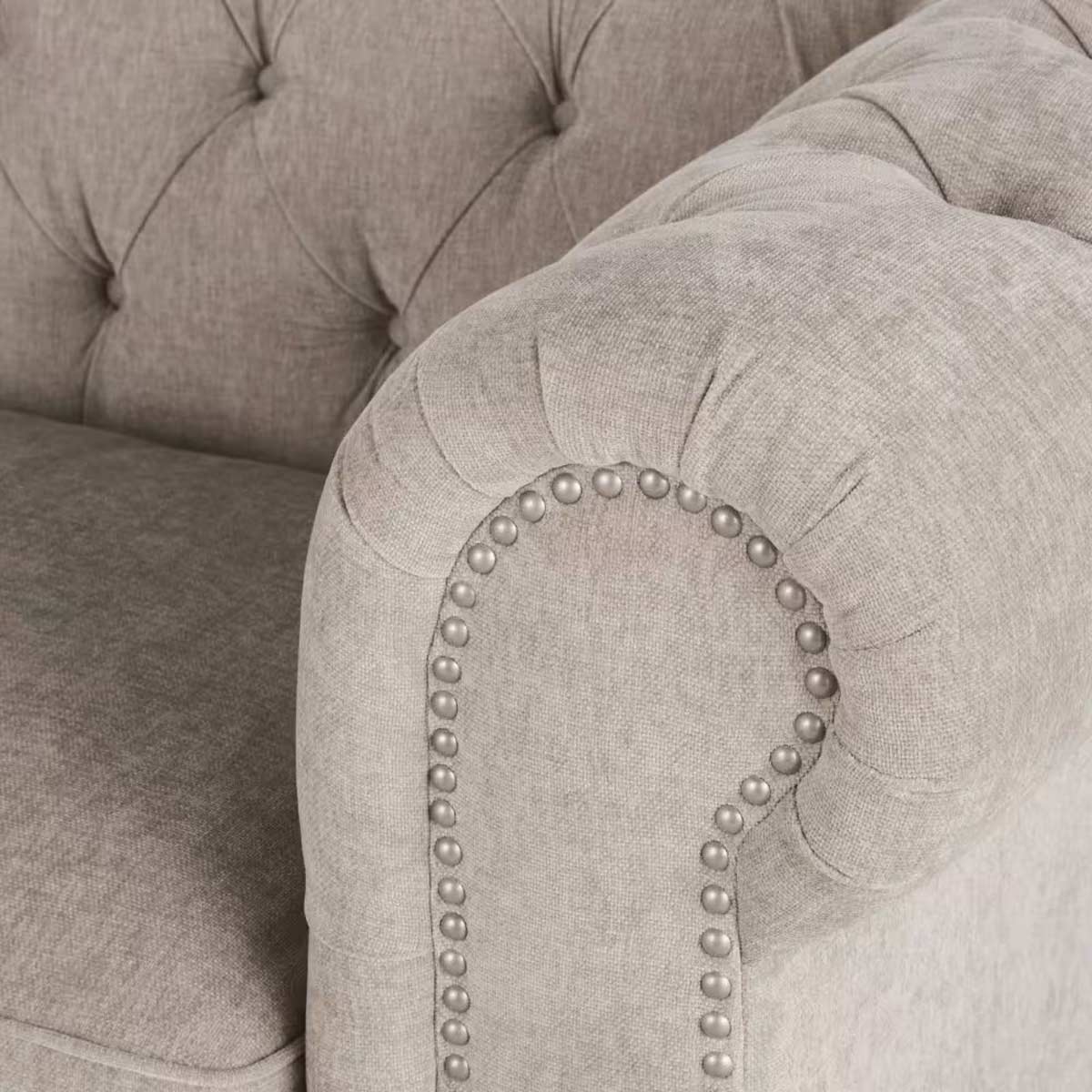 Dettaglio del bracciolo di un divano Chesterfield in velluto beige rosato, con lavorazione capitonné e borchie in acciaio anticato di Maisons du Monde.