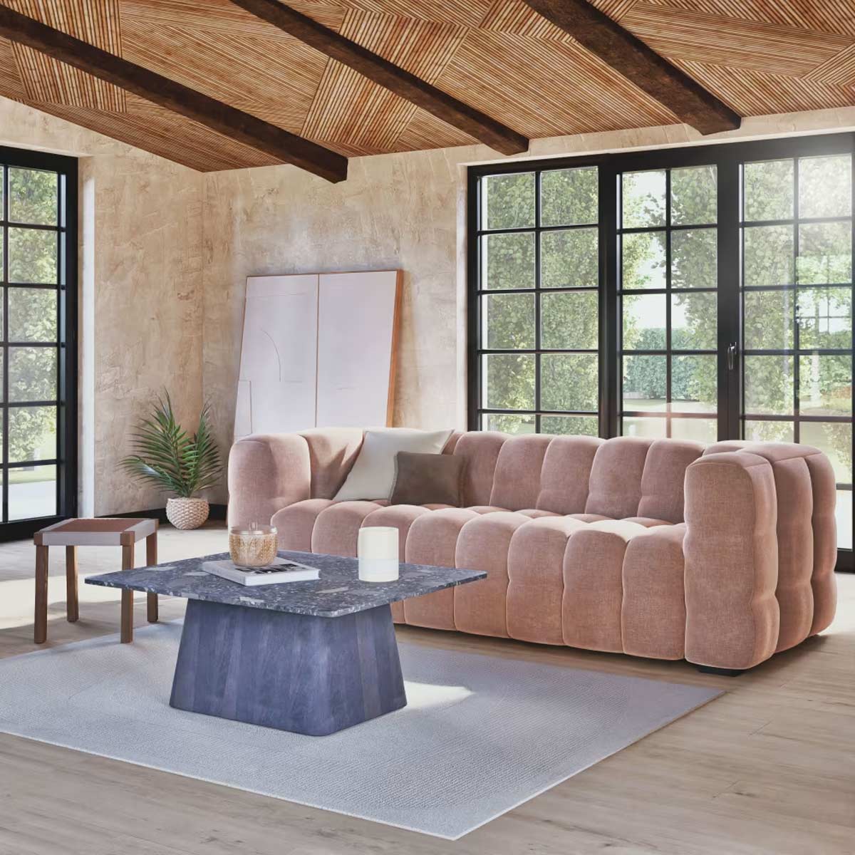 Divano Lilo in velluto caffellatte Maisons du Monde inserito in un salotto luminoso con grandi finestre, tavolo in pietra blu e soffitto in legno a vista.