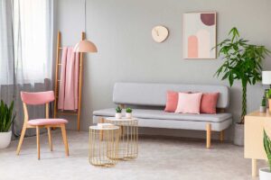 Soggiorno moderno con dettagli rosa cipria, arredi in legno chiaro e piante verdi, illuminato da luce naturale.