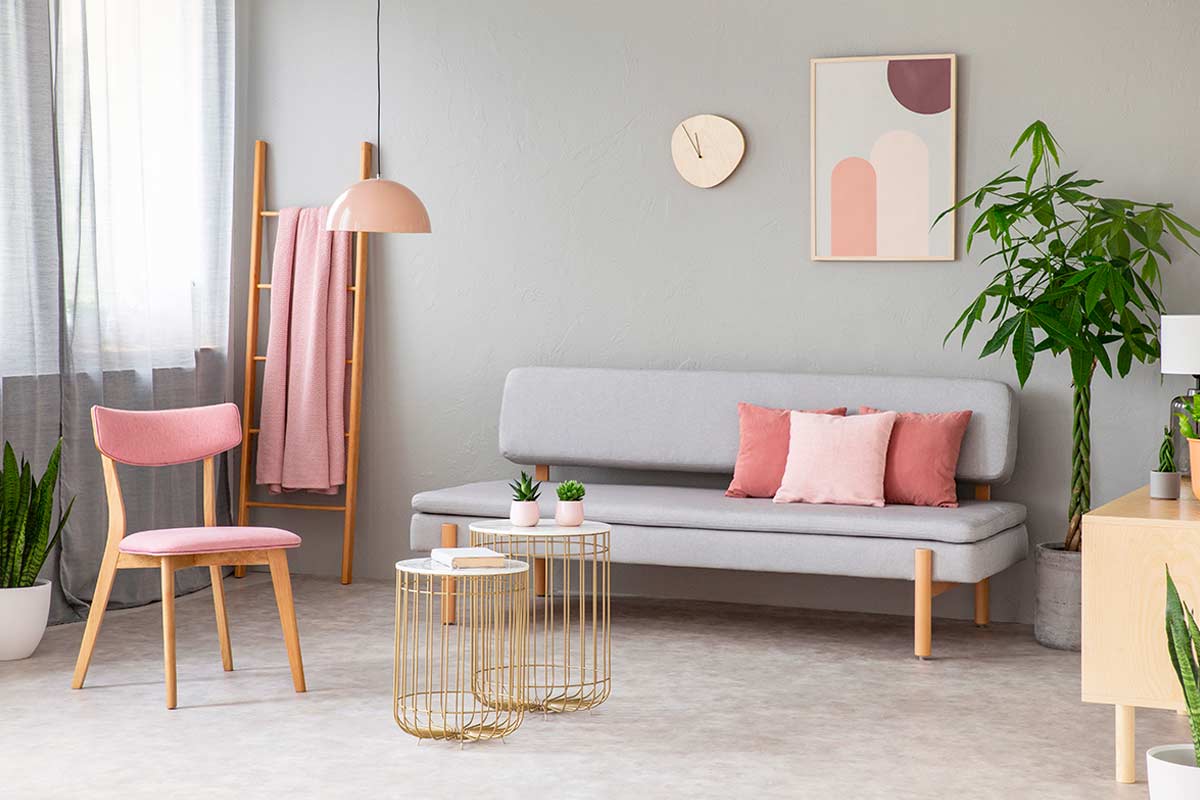 Soggiorno moderno con dettagli rosa cipria, arredi in legno chiaro e piante verdi, illuminato da luce naturale.