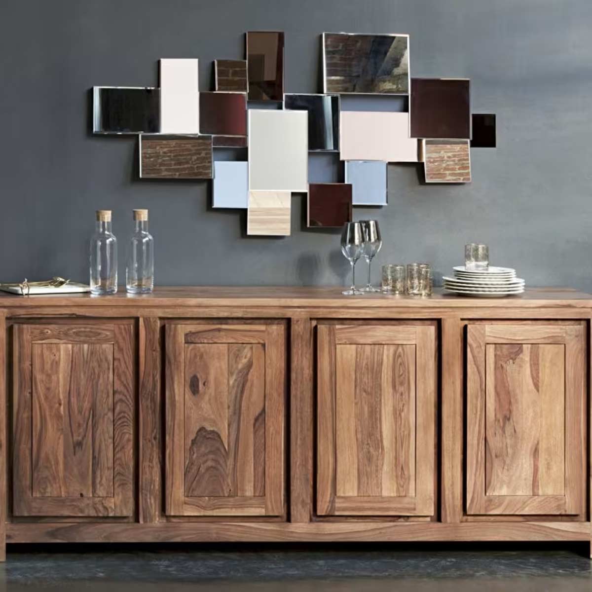 Madia in legno naturale con specchiera geometrica su parete grigia, bicchieri e piatti in stile moderno.