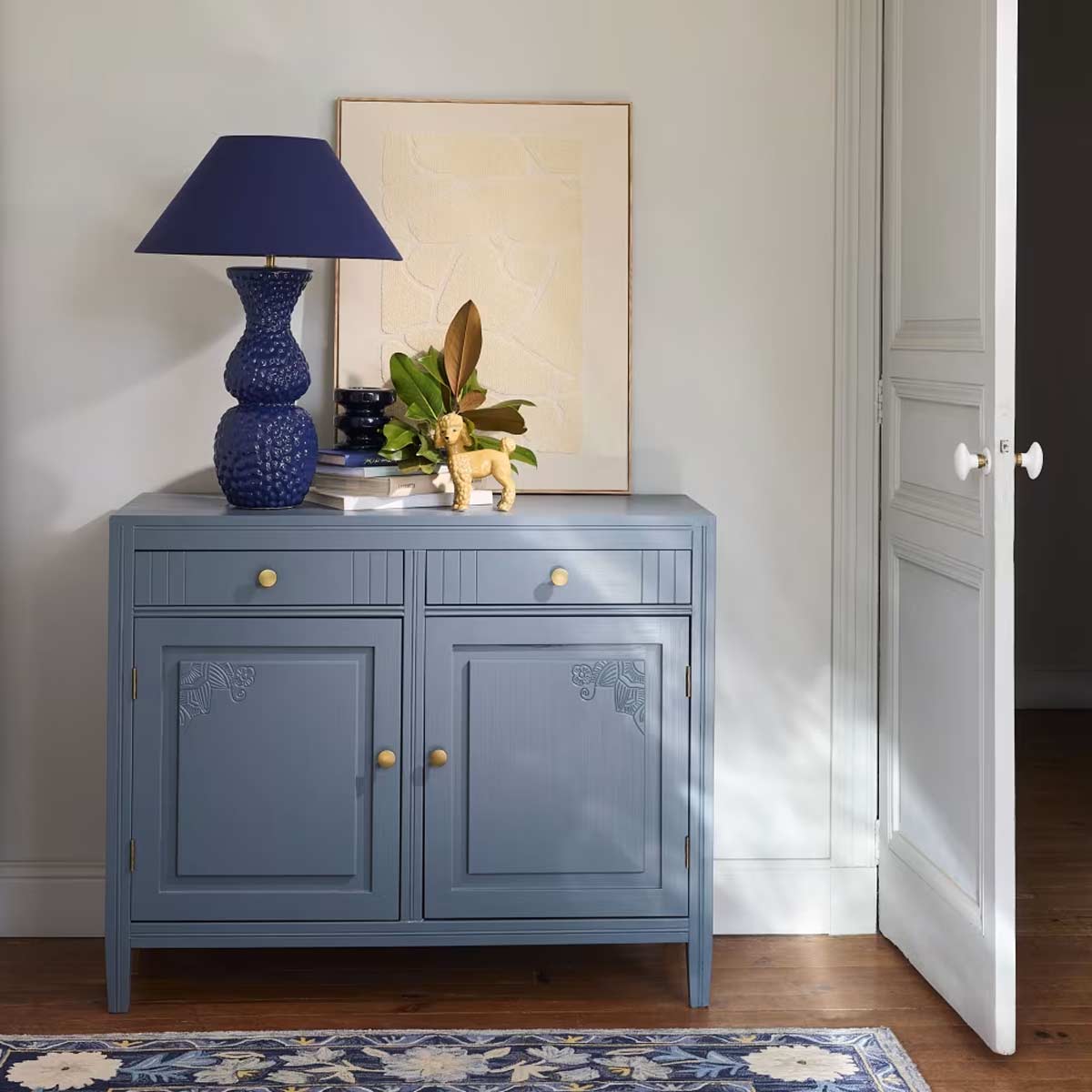 Madia blu in legno massello con pomelli dorati, ambientata in soggiorno luminoso dallo stile contemporaneo.