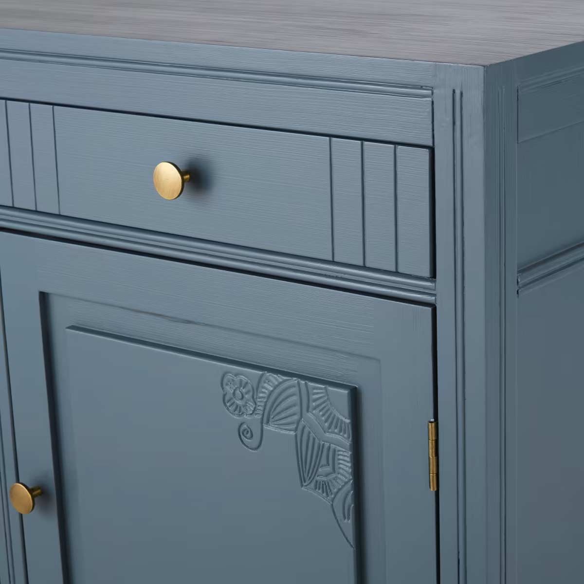 Dettaglio di una madia blu in legno massello con pomelli in ottone e incisioni decorative sugli angoli.