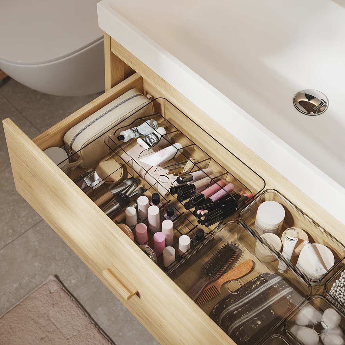 Dettaglio del cassetto del mobile lavabo IKEA RÅGRUND in bambù, organizzato con divisori e prodotti per la cura personale, trucchi e accessori da bagno ordinati.