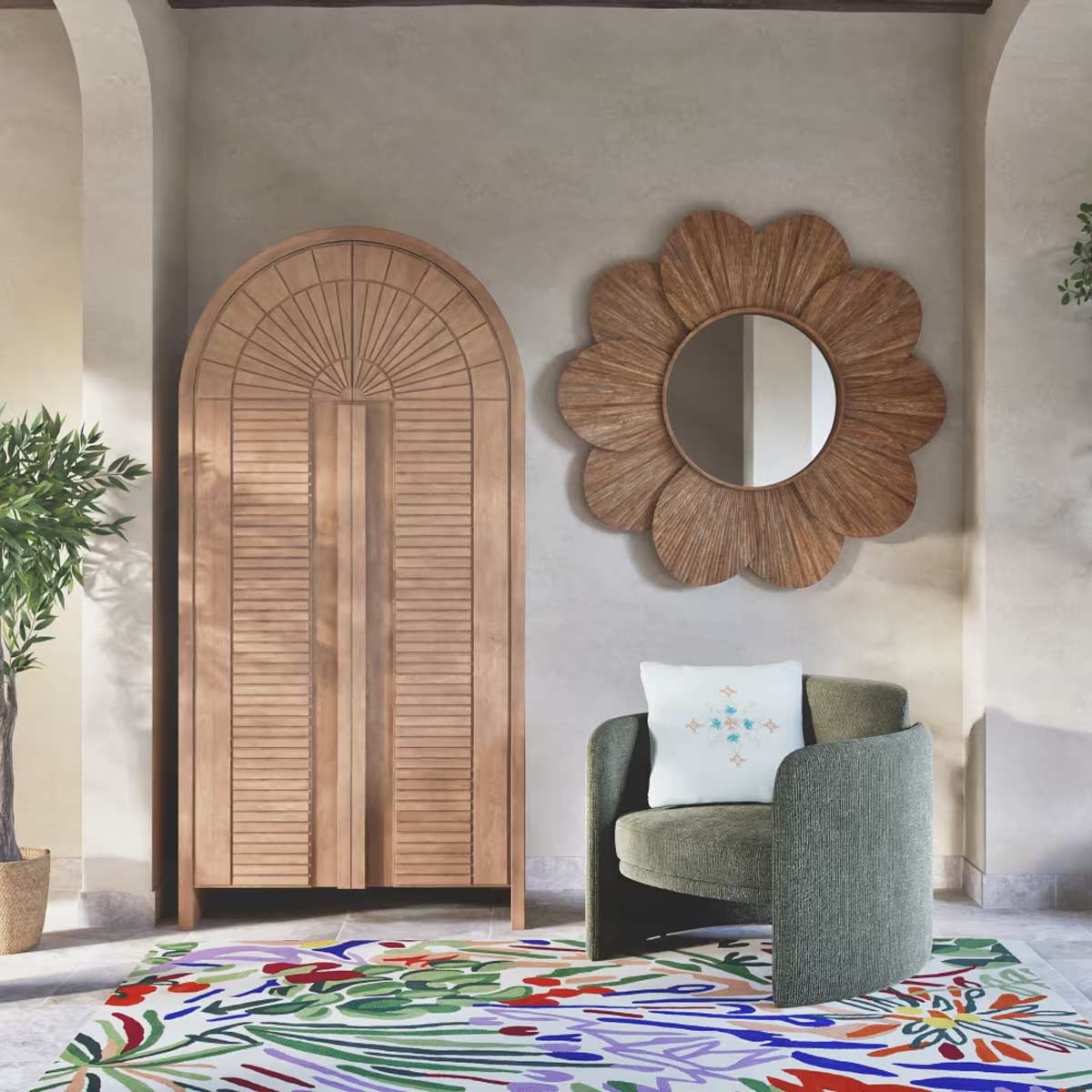 Poltrona Vegas Maisons du Monde in tessuto verde foresta inserita in soggiorno moderno, con specchio a forma di fiore, armadio in legno chiaro e tappeto colorato a motivi botanici.