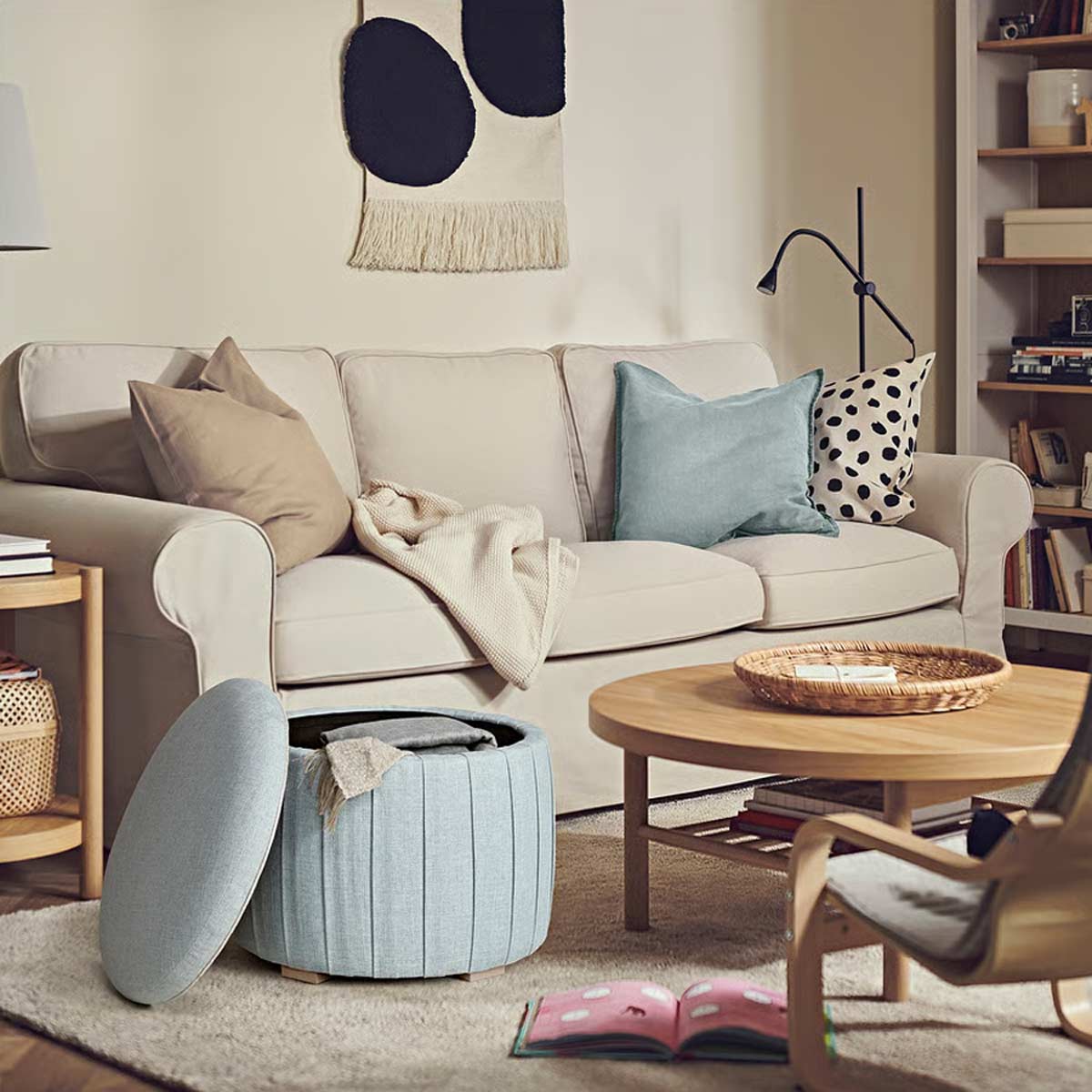 Pouf contenitore IKEA Kilanda azzurro aperto in salotto, davanti a divano beige e vicino ad un tavolino in legno chiaro, con plaid all’interno.