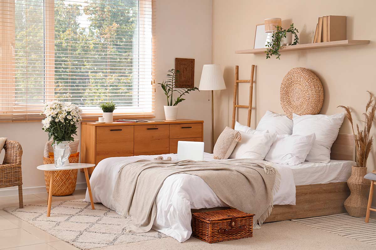 Camera da letto naturale con elementi asimmetrici sopra la testiera: disco di vimini, mensola, piante e lampada per una composizione equilibrata.