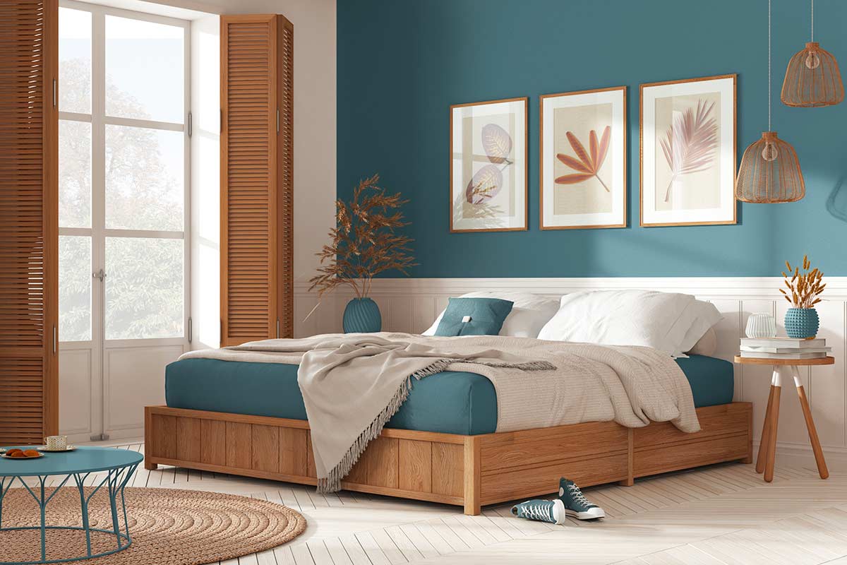 Camera da letto moderna con parete blu e tre quadri botanici allineati sopra la testiera in legno.