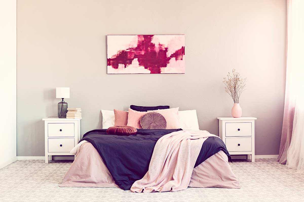 Letto matrimoniale con parete grigia e una tela panoramica astratta rosa sopra la testiera, arredo moderno e minimal.