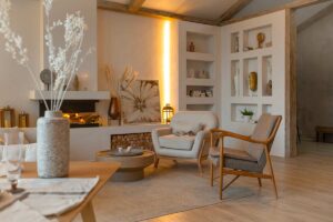 Salotto moderno con pareti chiare, poltrona in tessuto, tavolino basso in legno, vasi materici e illuminazione calda. Arredi essenziali e materiali naturali creano un’atmosfera rilassante e ordinata.